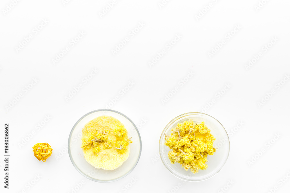 Aromatic spa salt. Yellow spa salt with delicate spring flowers on white background top view copy space Aromatic spa salt. Yellow spa salt with delicate spring flowers on white background top view copy space