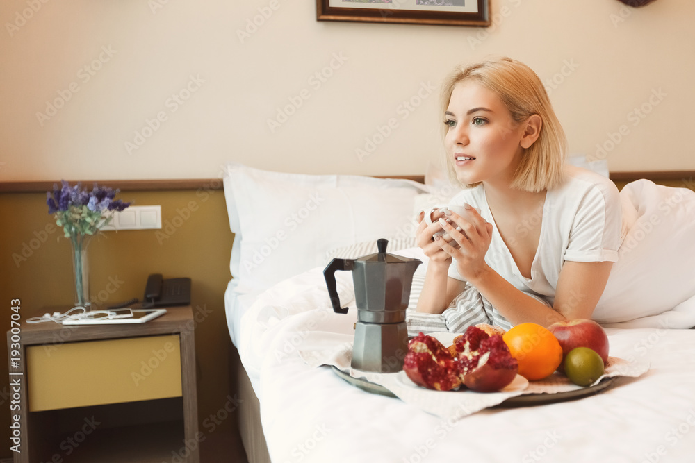 Beautiful young woman lying on bed and having breakfast