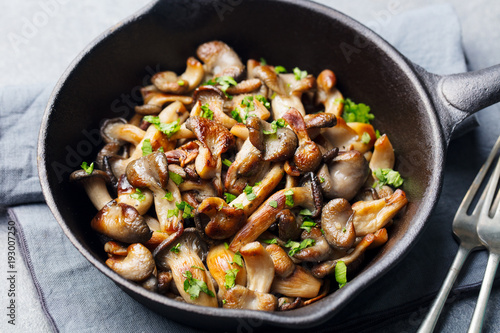 Fried mushrooms with fresh herbs in black cast iron pan.
