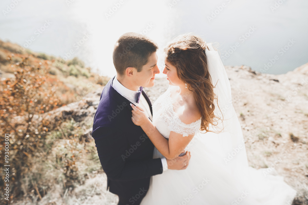 Wedding couple kissing and hugging on rocks near blue sea