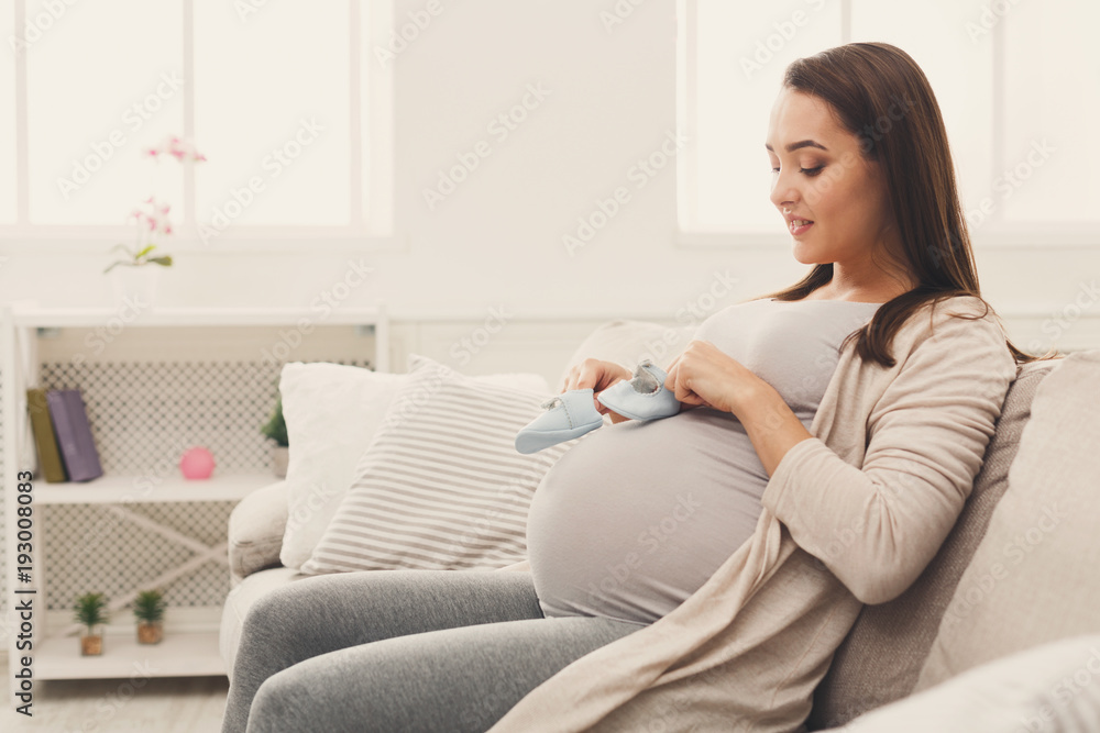 Pregnant woman holding tiny shoes near belly Pregnant woman holding tiny shoes near belly