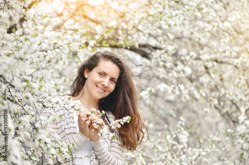 young woman stands near a blossoming tree in a spring park.