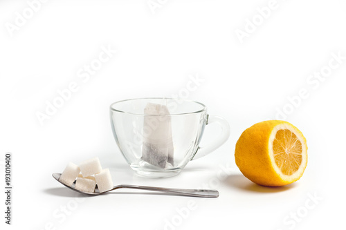 Glass cup for tea with a spoon, tea bag and lemon on a white background