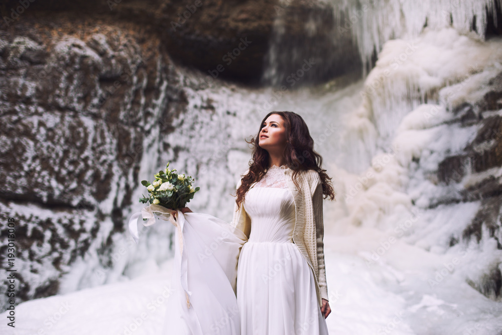 Young bride with a bouquet of flowers and a wedding dress on a background of a glacier in the mountains Young bride with a bouquet of flowers and a wedding dress on a background of a glacier in the mountains