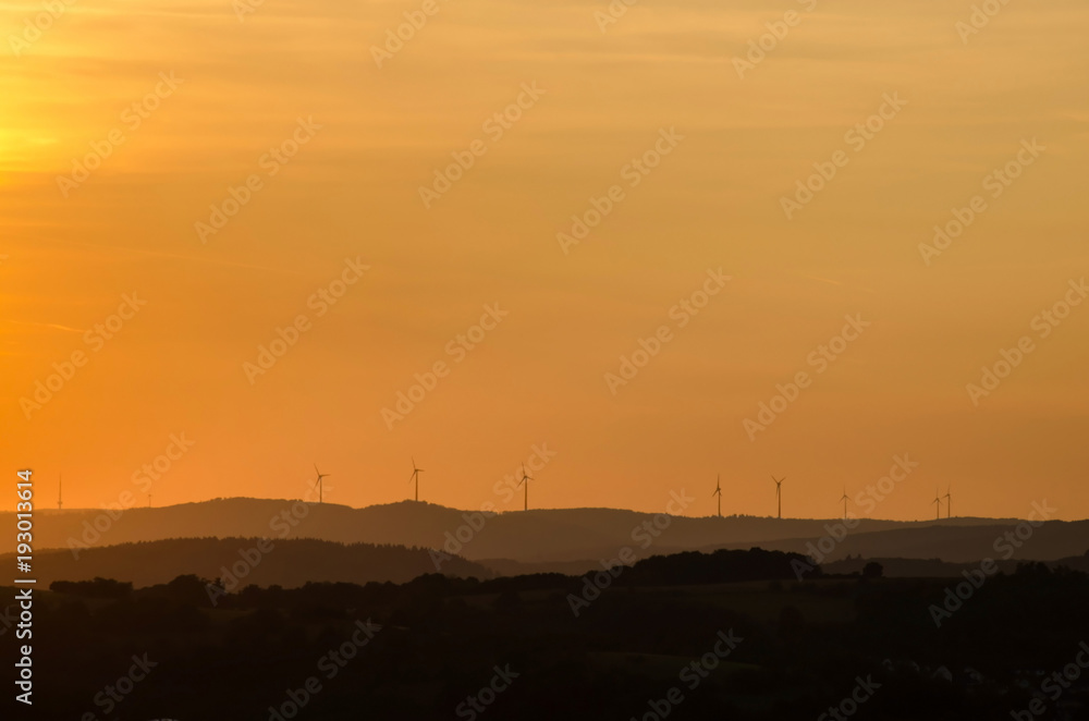 Sunset over Gladenbacher windpark. Silhouettes of wind generators on sunset background. Landscape.