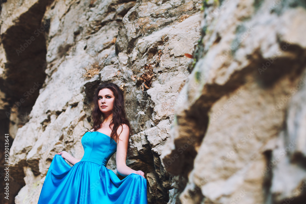 Beautiful young girl stands next to a mountain in a blue dress Beautiful young girl stands next to a mountain in a blue dress