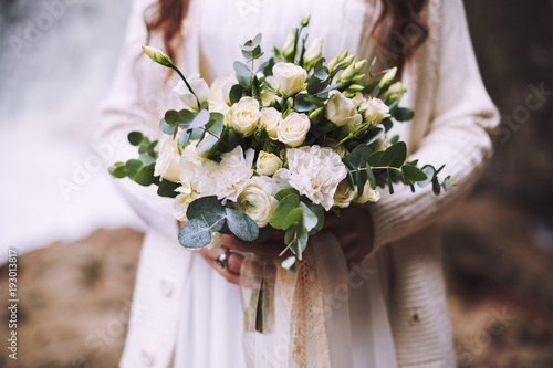 A girl is holding a wedding bouquet of flowers against the background of a glacier