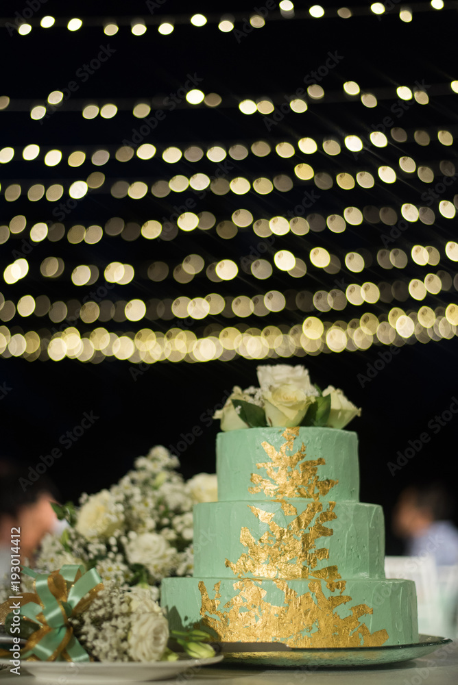 three layers green color cake with white rose on top and beautiful bokeh on background