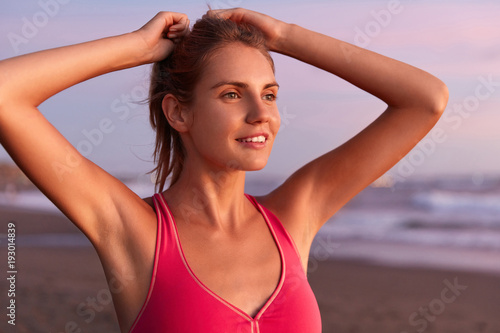 Active female model has training outdoor for keeping good shape body, runs across seashore, has workout in morning, admires beautiful landscape and fresh breeze. Fitness and motivation concept