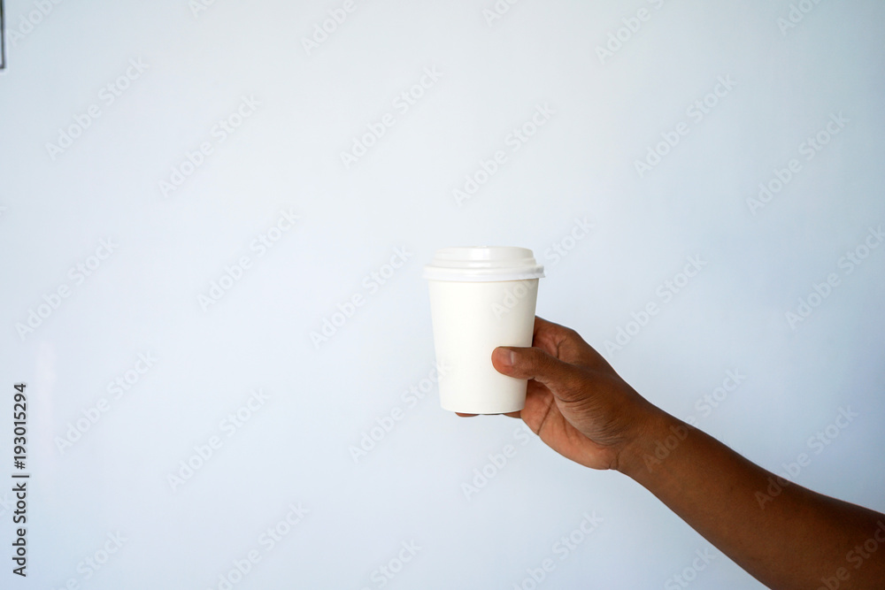The hand of a dark-skinned man holds a disposable cup for coffee or tea background a white and blue wall. Side view with copy space The hand of a dark-skinned man holds a disposable cup for coffee or tea background a white and blue wall. Side view with copy space