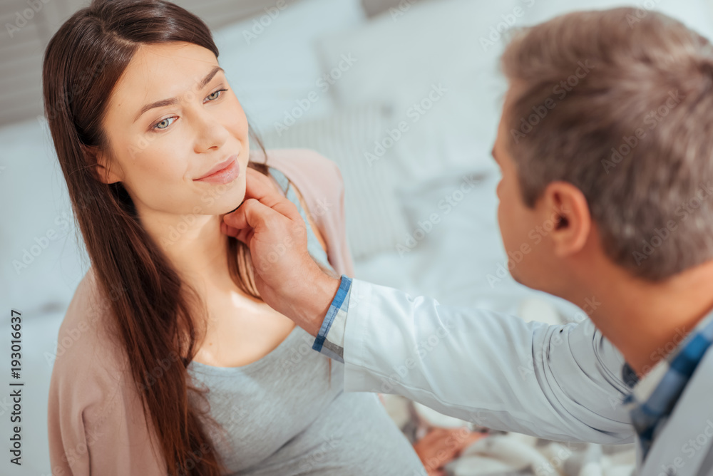 Healthy and happy. Selective focus on a charming pregnant woman smiling while visiting her doctor and listening to him. Healthy and happy. Selective focus on a charming pregnant woman smiling while visiting her doctor and listening to him.