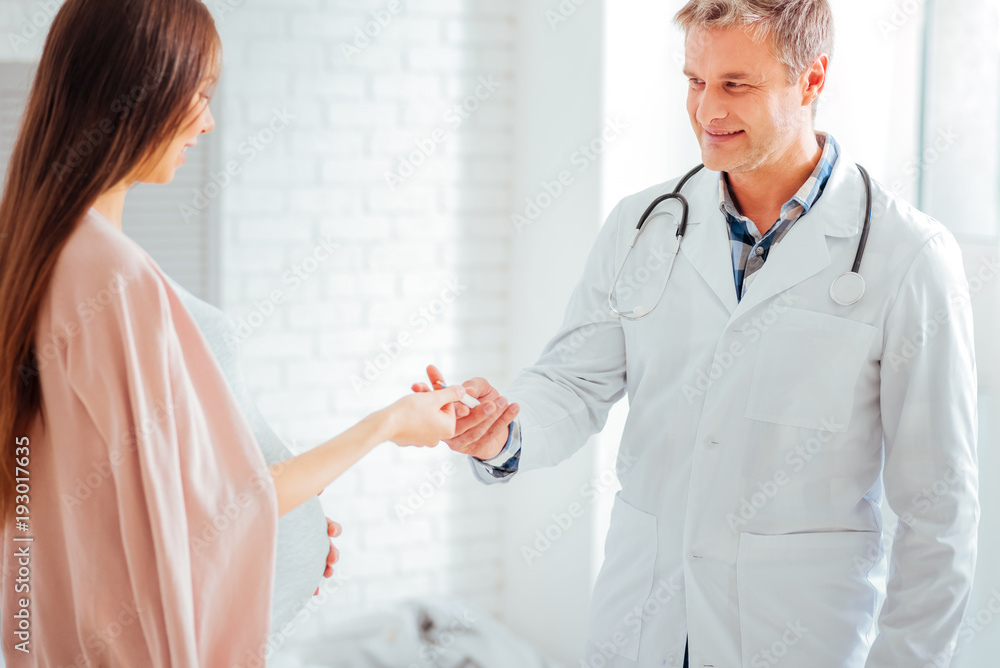 Do not forget about the temperature. Smiling pediatrician looking at an expectant mother while giving her a thermometer during an appointment. Do not forget about the temperature. Smiling pediatrician looking at an expectant mother while giving her a thermometer during an appointment.