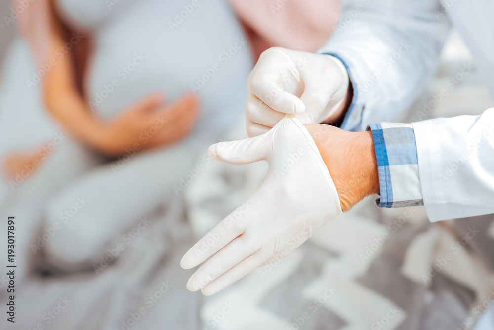 Getting ready. Scaled up look on a male medical worker putting on his rubber gloves while preparing for an appointment. Getting ready. Scaled up look on a male medical worker putting on his rubber gloves while preparing for an appointment.