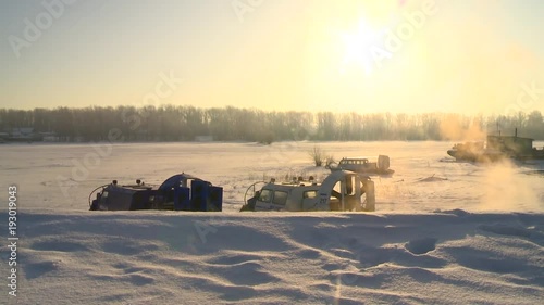  two small ships on the air cushion stand with the engine running, smoke comes out of the exhaust pipe, snow around it and the sun is shining photo