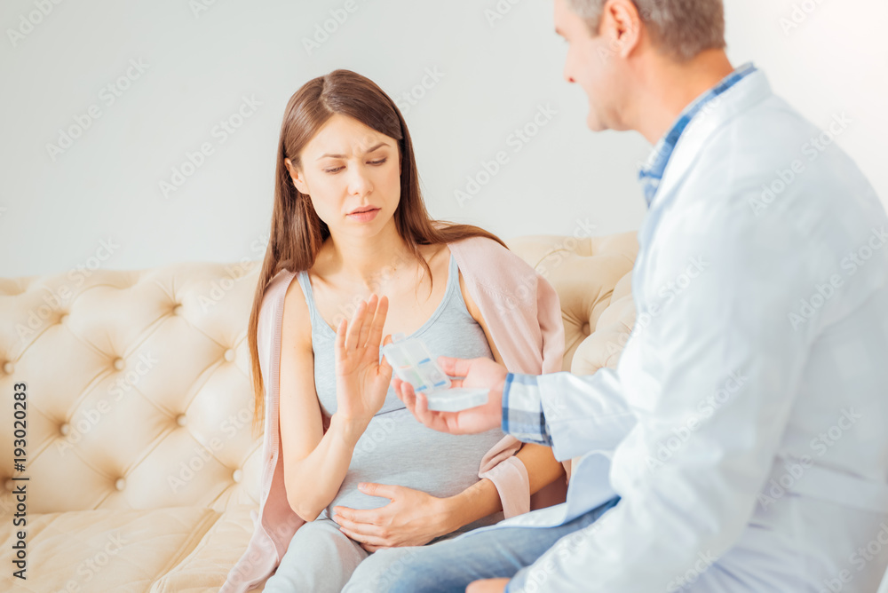 Fototapeta premium Its enough. Serious concentrated pregnant woman sitting near a doctor protesting and gesticulating.