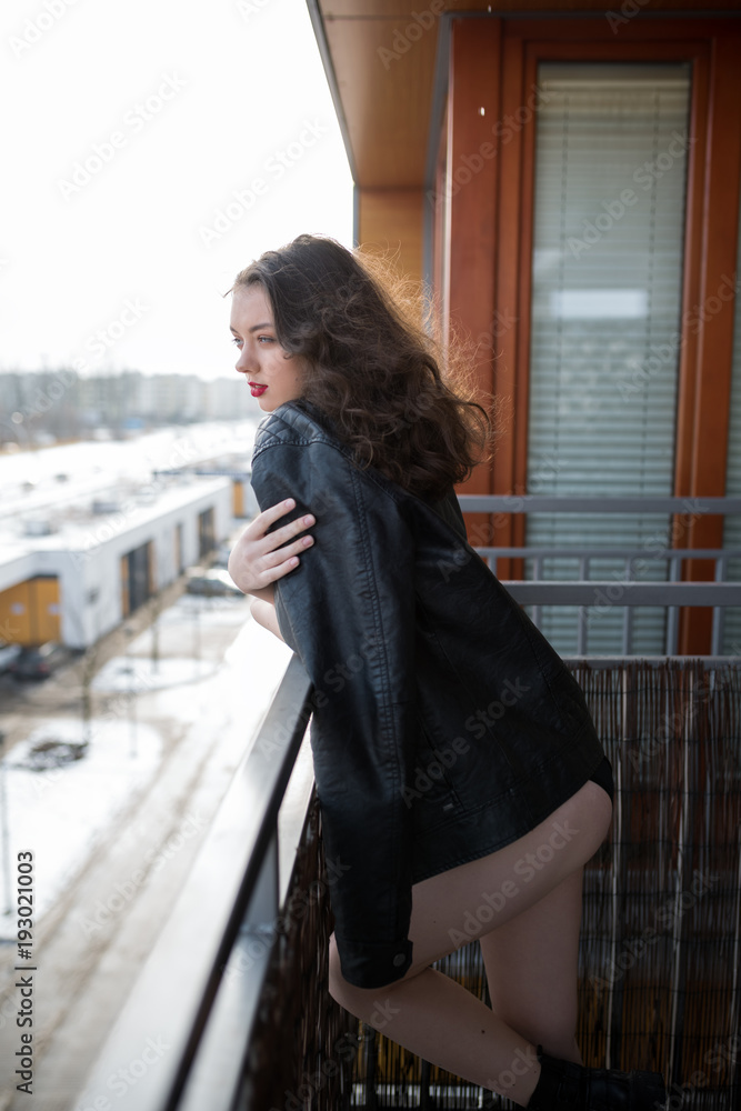 Young sexy woman in a jacket fur coat and lingerie standing on balcony