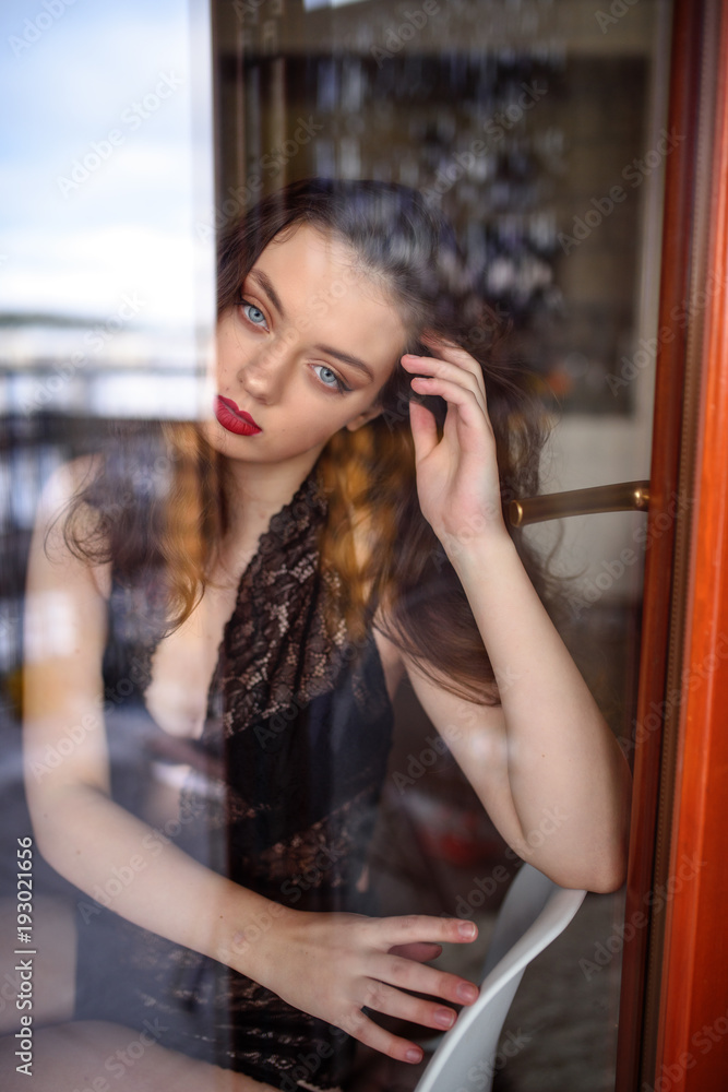 Young sexy woman in black lingerie poses outside the window. Reflection effects
