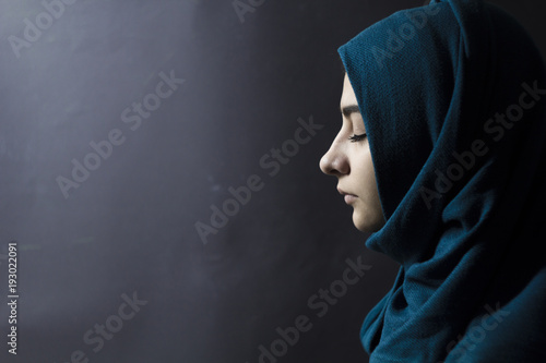 A Muslim woman with closed eyes, on a black background. Arab girl in hijab in profile.