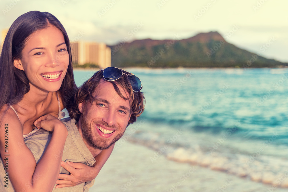 Happy interracial couple, woman piggybacking on man on Waikiki beach with Diamond Head Mountain landscape. Healthy people portrait, Honolulu, Hawaii. Travel holidays destination.