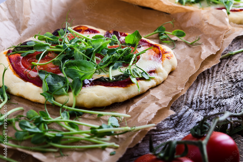 Homemade pizza with tomatoes and sprouts topping on rustic table Homemade pizza with tomatoes and sprouts topping on rustic table