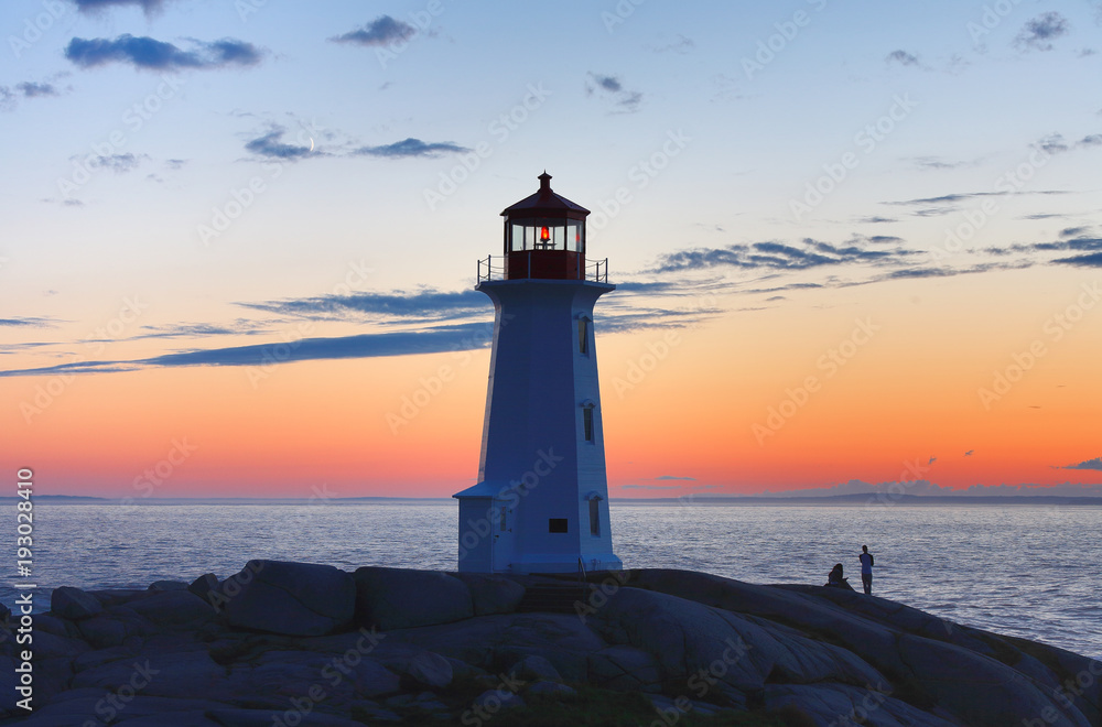Beautiful Peggy Cove Light House with Sunset, Nova Scotia, Canada. Photo shows tourists watching sunset.