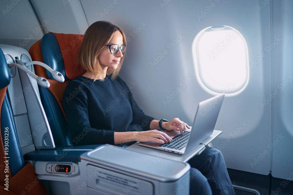 Obraz premium Podróżowanie i technologia. Latanie w pierwszej klasie. Ładna młoda businees kobieta pracuje na laptopie podczas gdy siedzący w samolocie.