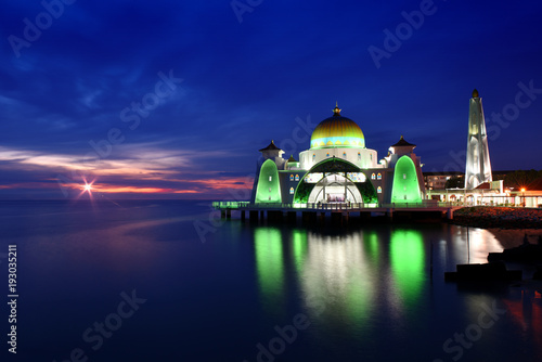 Glowing Strait Mosque of Malacca during sunset and blue hour. The so called swimming Mosque is located at the Historical Malacca City, Malaysia.