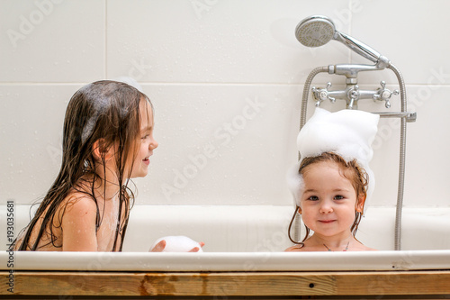 Two little sisters play in a bath.