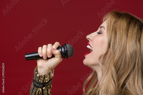 Side view profile of peaceful lady holding mike and singing with eyes closed. Isolated on red background