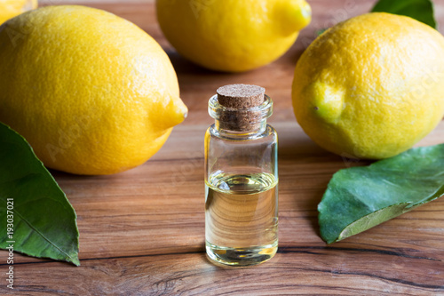 A bottle of lemon essential oil with fresh lemons and leaves photo