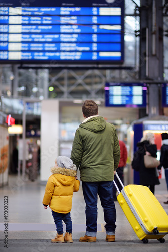 Little boy and his father in international airport or on railway station platform looking on information display