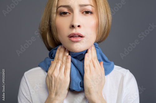 Cuadro en lienzo Portrait of sick sad woman in scarf wrapped around her neck, she is touching her throat and looking at camera