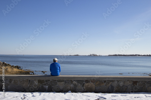 man on his own  sitting on a wall looking out to sea