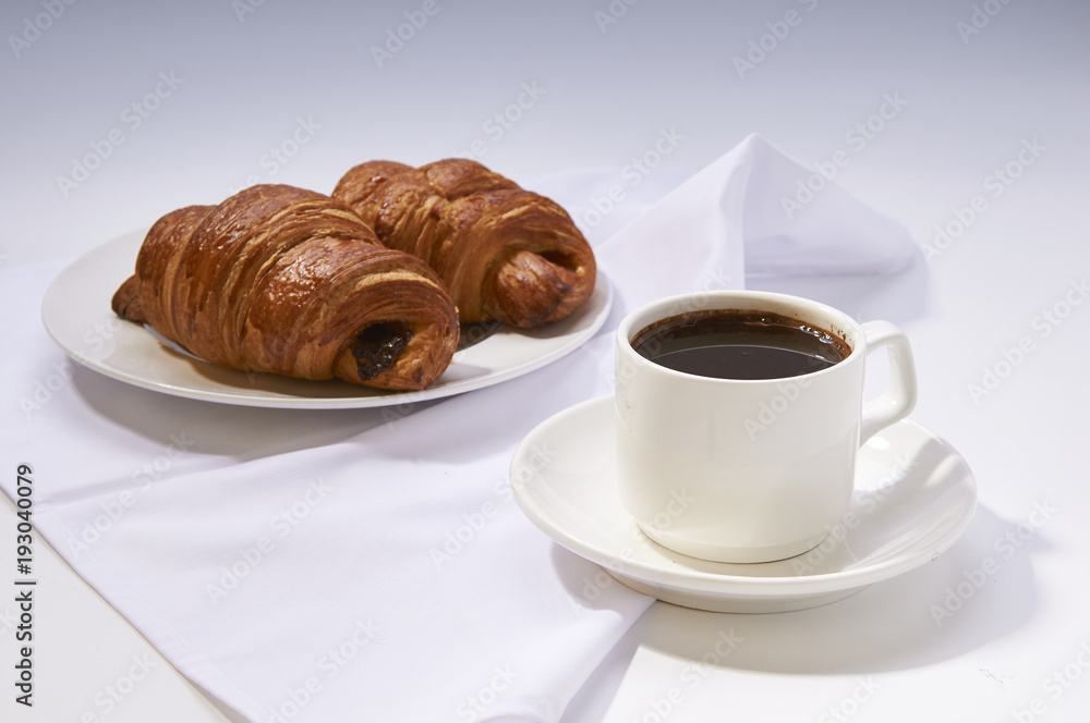 Coffee cup with croissant. Breakfast meal with fresh coffee and french pastry on white Coffee cup with croissant. Breakfast meal with fresh coffee and french pastry on white