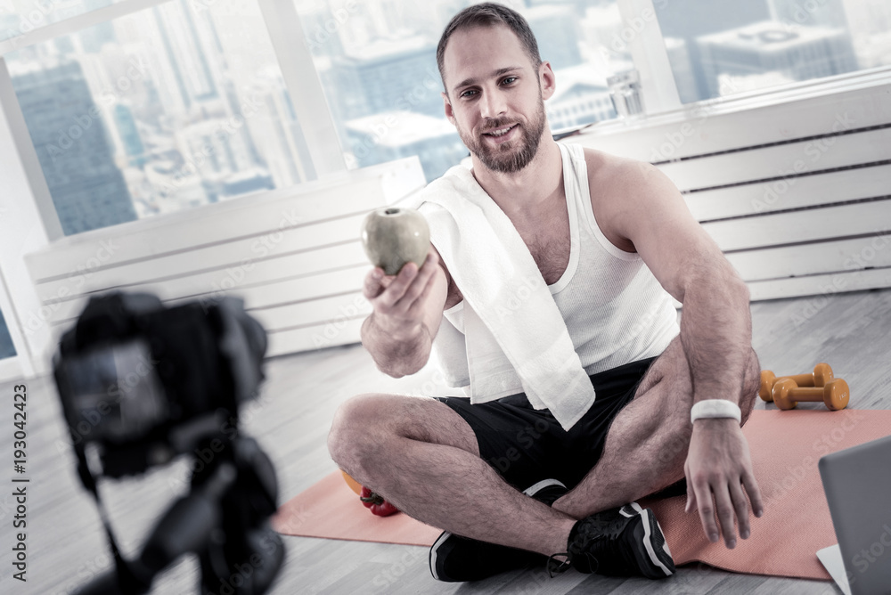 Obraz premium Apple for day. Bearded charming male blogger creating blog while sitting on mat board and stretching apple