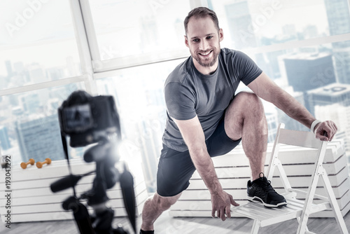 Excellent motivation. Cheerful pretty male blogger putting leg on chair while showing technique and smiling