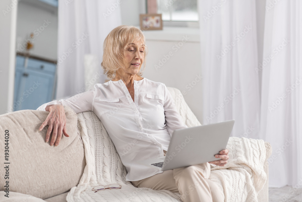 Whats new. Nice pensive mature woman placing laptop on knees while sitting on couch and gazing at screen Whats new. Nice pensive mature woman placing laptop on knees while sitting on couch and gazing at screen
