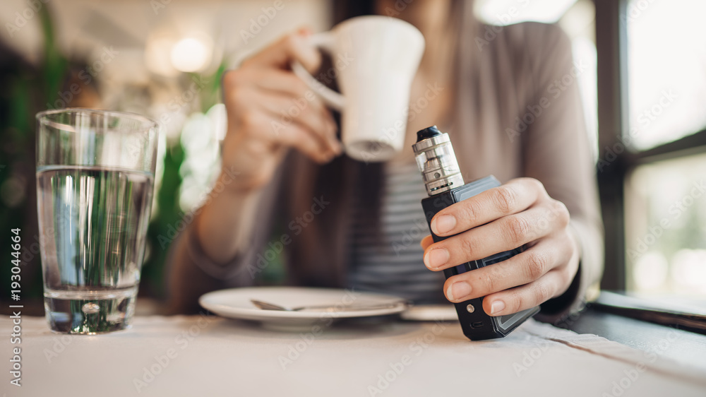 Young woman using electronic cigarette to smoke in public places.Smoke restriction,smoking ban.Using vaping device with flavoured liquid.E-juice vaping.Smoking habit,nicotine addict,tobacco industry Young woman using electronic cigarette to smoke in public places.Smoke restriction,smoking ban.Using vaping device with flavoured liquid.E-juice vaping.Smoking habit,nicotine addict,tobacco industry