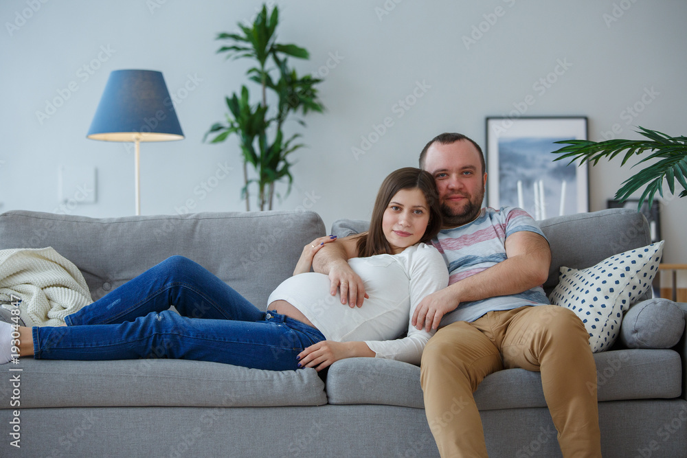 Photo of happy pregnant woman and man on gray sofa Photo of happy pregnant woman and man on gray sofa