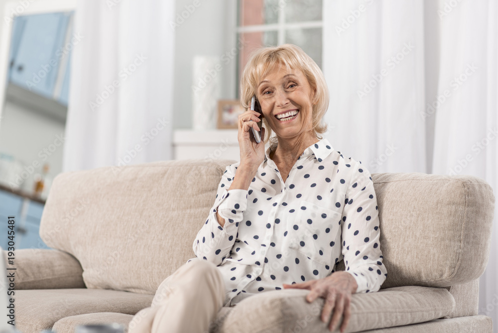 Timeless talk. Adorable joyful mature woman sitting on coach while making call and laughing Timeless talk. Adorable joyful mature woman sitting on coach while making call and laughing