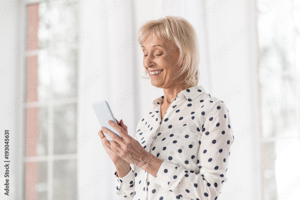 Happy moment. Happy attractive mature woman working on phone while gazing at screen and laughing Happy moment. Happy attractive mature woman working on phone while gazing at screen and laughing