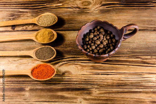 Ceramic bowl and spoons with the different spices on wooden table