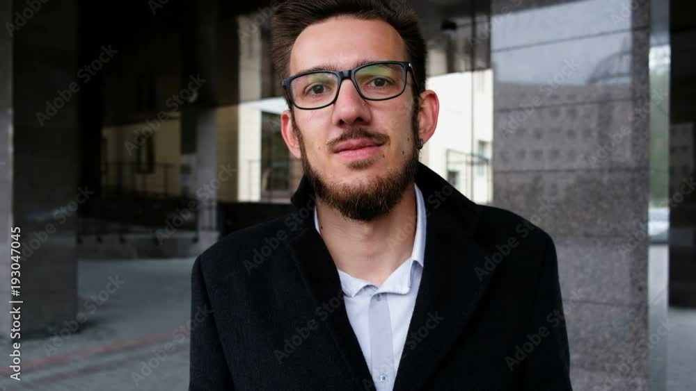 Portrait of a young successful manager in a classic suit, glasses and looks at the camera. With corporate or business building in background Portrait of a young successful manager in a classic suit, glasses and looks at the camera. With corporate or business building in background