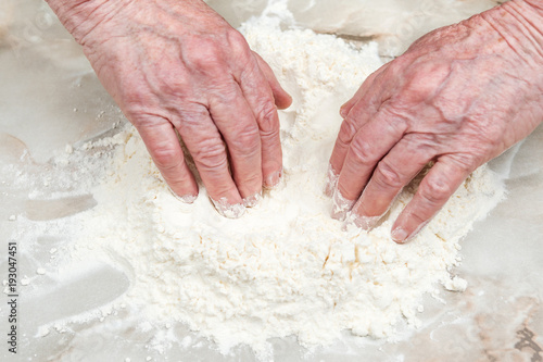 Hands of the old woman make a hole in the flour scattered on the table