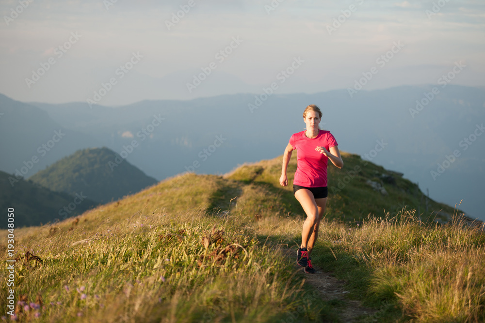 Woman runs on a top of the mountains with mountain range in background