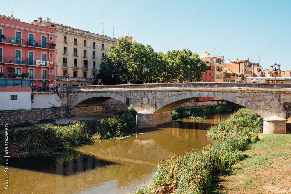 Obraz premium Colorful yellow and orange houses and bridge Pont de Sant Agusti reflected in water river Onyar, in Girona, Catalonia, Spain.