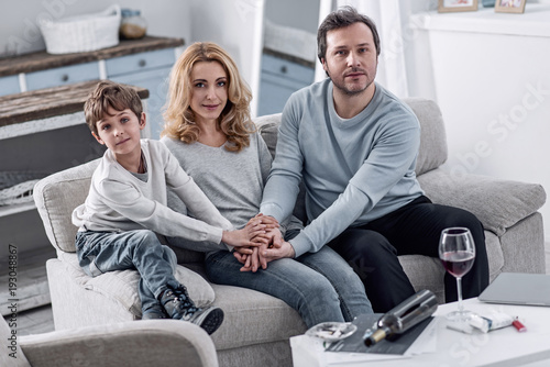 Feeling good. Young calm woman sitting between her kind little son and a loving husband while holding their hands and thinking about the future without alcohol addiction