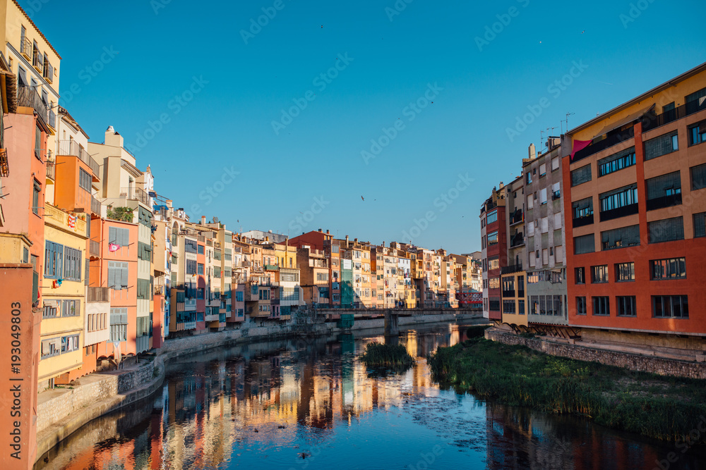 Colorful yellow and orange houses and bridge Pont de Sant Agusti reflected in water river Onyar, in Girona, Catalonia, Spain.