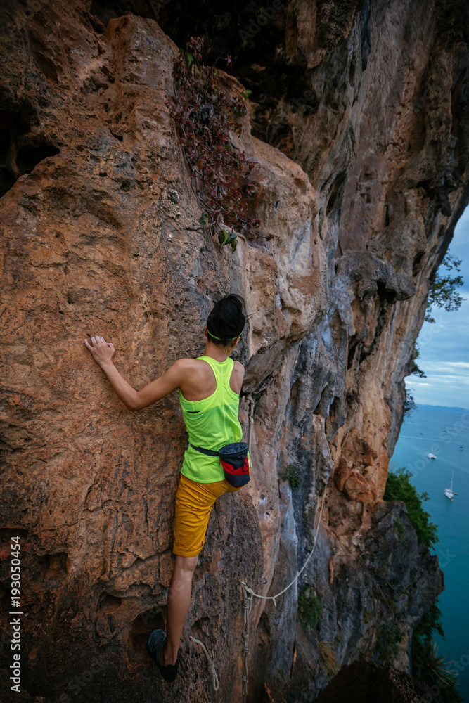female rock climber climbing on seaside cliff