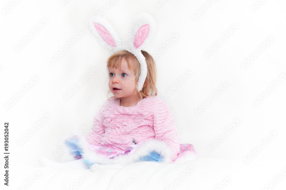 Fototapeta premium Closeup Portrait of Blonde Baby 18 month old Girl with Big Blue Eyes and Bunny Ears headband, Pink Tutu, isolated on white background.